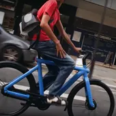 A man on a blue e-bike glancing back while riding through a city street