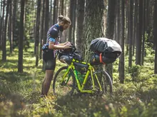 A cyclist packing bags onto a loaded touring bike in a pine forest