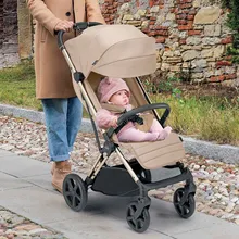 A woman in a camel coat pushing a baby in a beige stroller along a cobbled path